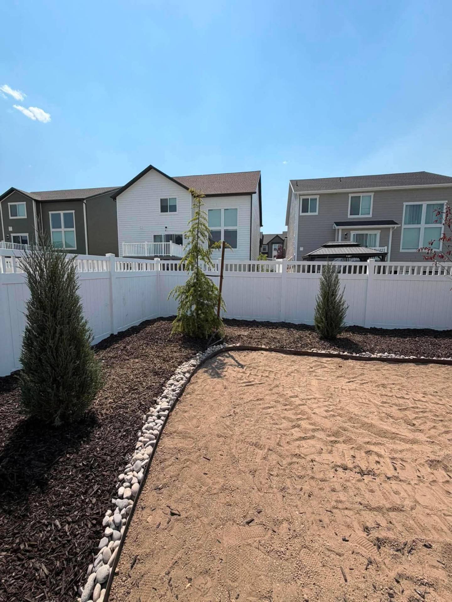Finished Summit Landscape & Excavation backyard install in Utah County with vinyl fence, mulched beds, river rock border, and arborvitae plantings