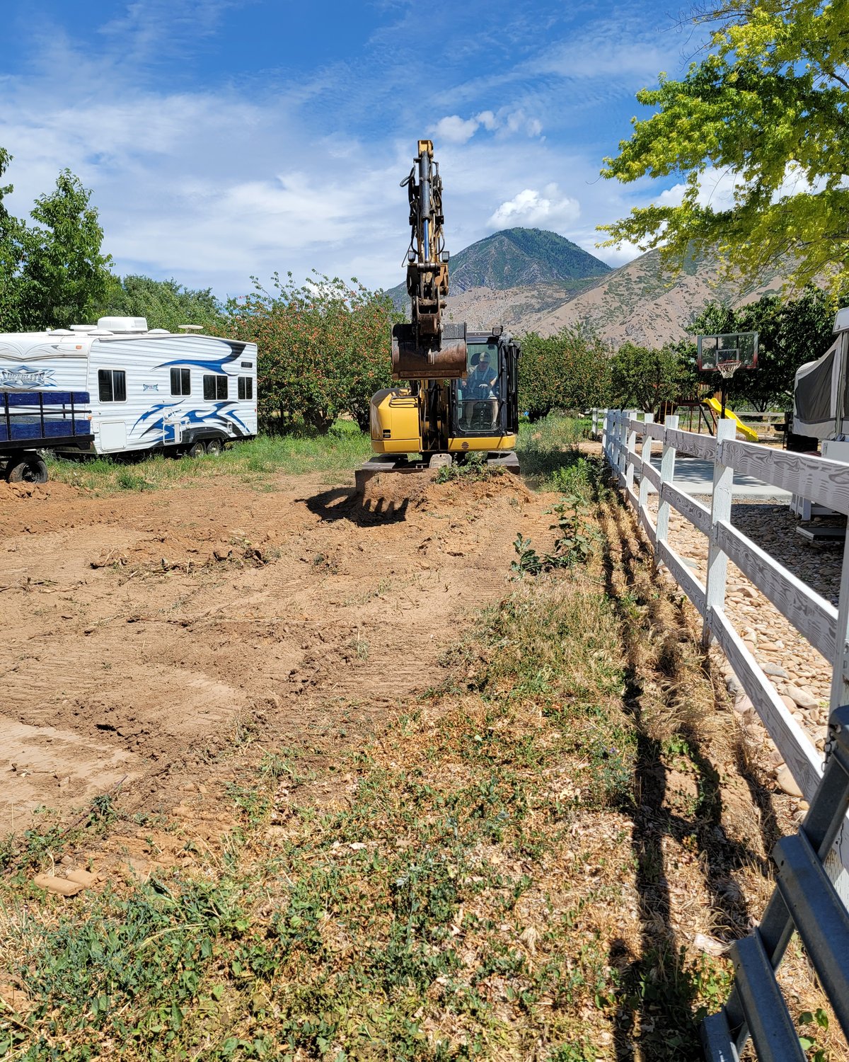 Excavator grading next to a white fence